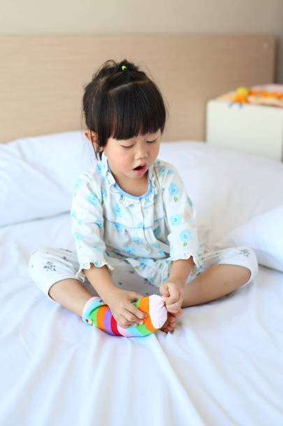 Adorable little girl trying to put a socks on the bed. - Foto, Imagem