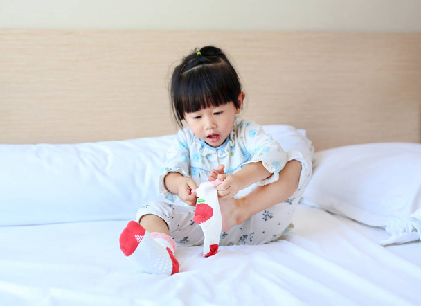 Adorable little girl trying to put a socks on the bed. - Fotó, kép