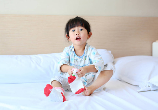 Adorable little girl trying to put a socks on the bed. - Photo, Image
