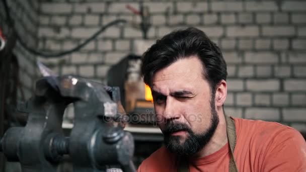 Kowal pochyla Metalowy nóż z narzekać w warsztacie forge, portret - Materiał filmowy, wideo