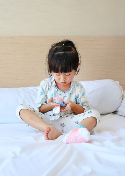 Rozkošná holčička se snaží dát ponožky na postel. - Fotografie, Obrázek