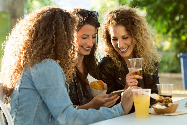 Trois belles jeunes femmes utilisant leur téléphone portable dans la rue
. - Photo, image