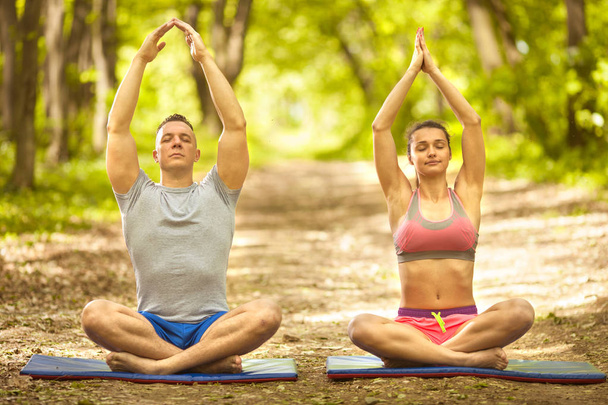 young couple relaxing in yoga pose in green nature - 写真・画像