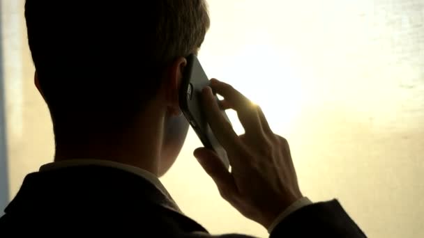 Young man in suit talking on cellphone near window at home. Close up. Back shot - Πλάνα, βίντεο