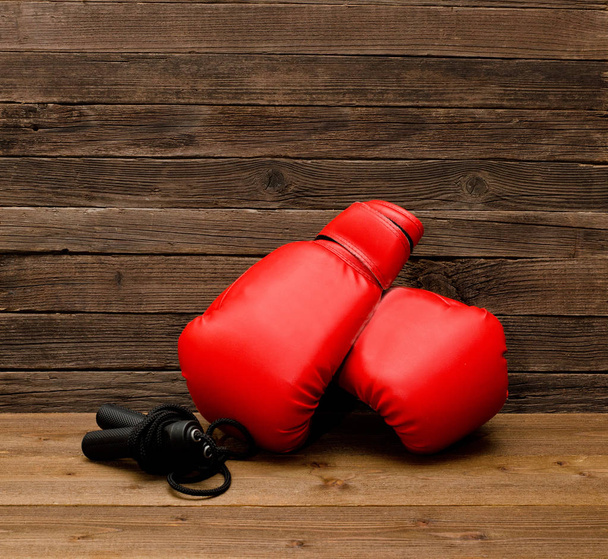 Dvě červené Boxerské rukavice leží na dřevěné hnědé pozadí, přeskakování lana prázdné místo - Fotografie, Obrázek