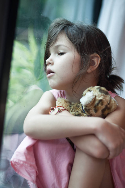 κορίτσι που κάθεται κοντά σε παράθυρο με το παιχνίδι - Φωτογραφία, εικόνα
