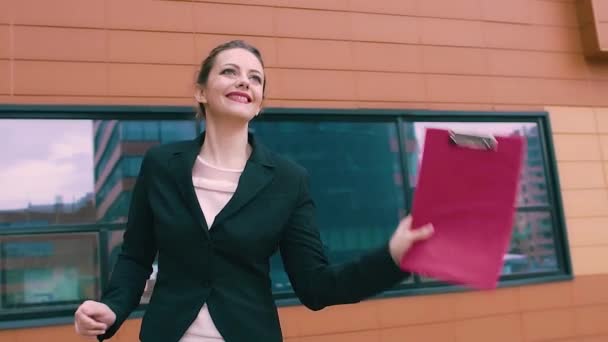 Smiling girl is happy and incendiary dances. beautiful woman on the background of the business building. SLOW MOTION - Materiał filmowy, wideo