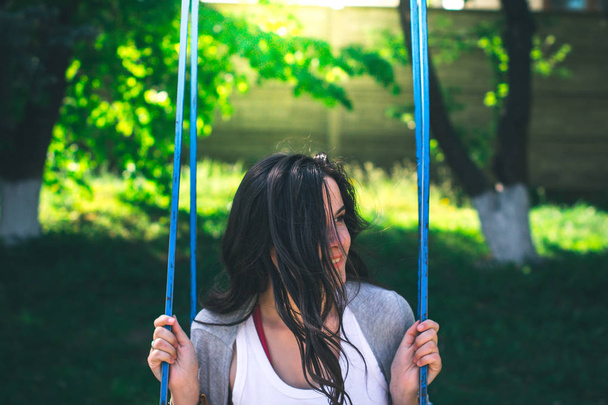 Young beautiful girl on a swing in the park emotions concept. - 写真・画像