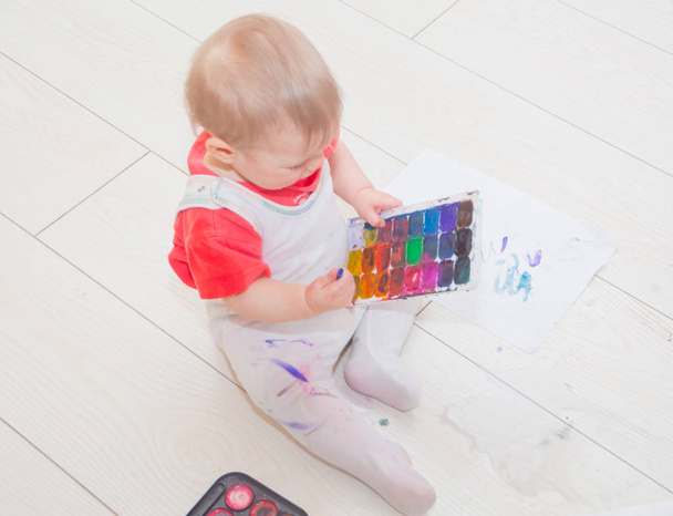 a baby with a brush and paints on clothes. - Фото, изображение