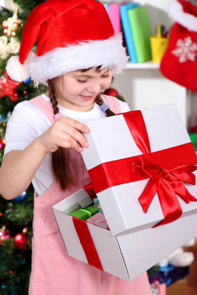 A little girl opens a gift in festively decorated room - Foto, Imagem