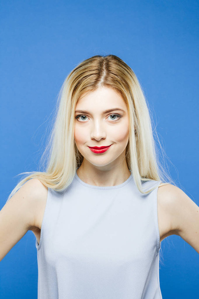 Front View of Amazing Pretty Woman with Long Hair Having Fun in Studio. Portrait of Smiling Blonde Wearing Elegant Dress on Blue Background. - Foto, Imagem
