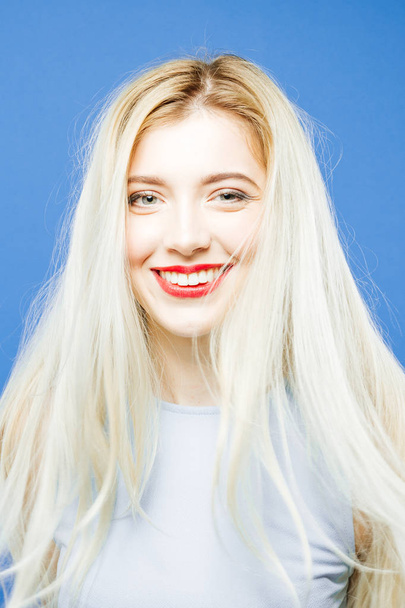 Woman with Toothy Smile on Blue Background. Portrait of Girl with Long Hair Wearing Elegant Dress and Having Fun in Studio. - Фото, изображение