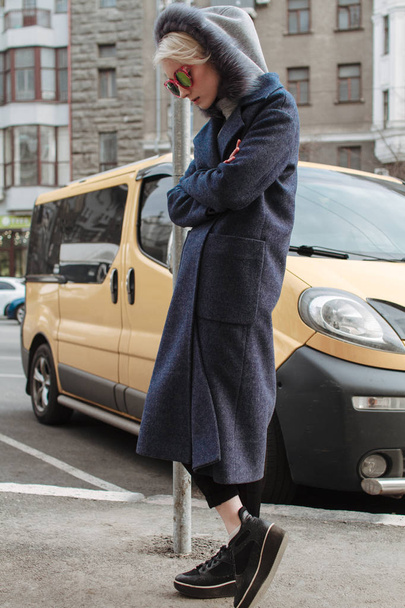 Una chica rubia con gafas y un abrigo pasea por las calles de la ciudad
 - Foto, imagen