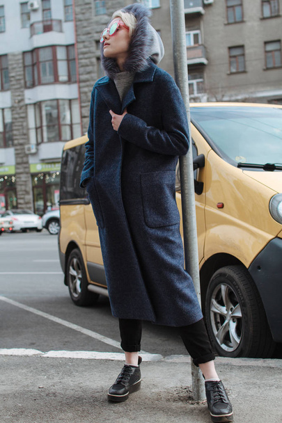 Uma menina loira com óculos e um casaco caminha pelas ruas da cidade
 - Foto, Imagem