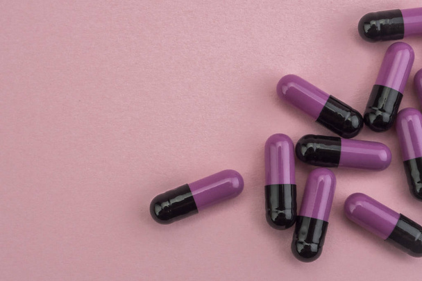 Багато ліків фіолетові і чорні таблетки капсули на рожевому фоні
 - Фото, зображення