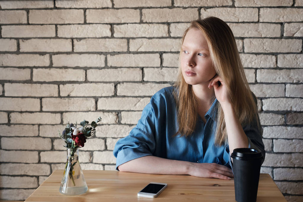 Young blonde in blue shirt sits at the table in a cafe on which  - Photo, image