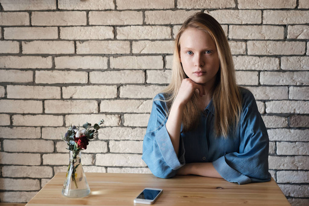 A blonde girl in blue shirt sits at the table in a cafe and look - Фото, зображення