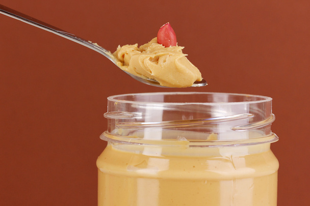 Delicious peanut butter in jar and spoon on brown background - Φωτογραφία, εικόνα