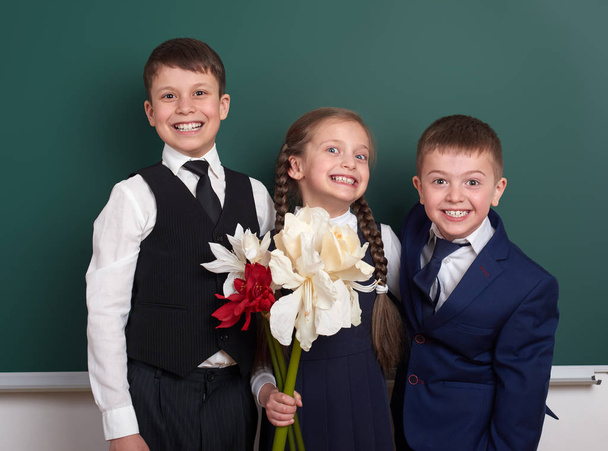 jongens geven meisje bloemen, basisschool kind in de buurt van leeg schoolbord achtergrond, gekleed in een klassieke zwarte pak, leerling van de groep, onderwijs concept - Foto, afbeelding
