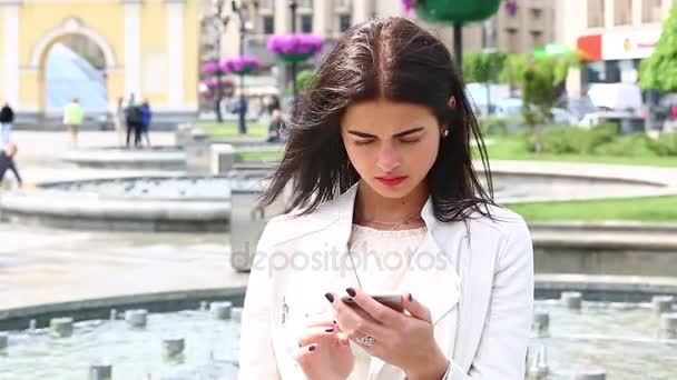 Πορτραίτο κοριτσιού γελώντας χρησιμοποιώντας το smartphone. Όμορφη νεαρή γυναίκα με το κινητό της τηλέφωνο σε φόντο κρήνη. Αρκετά ευτυχισμένη γυναίκα χρησιμοποιώντας το smartphone στο Δημοτικό Πάρκο Steadicam πυροβόλησε. - Πλάνα, βίντεο