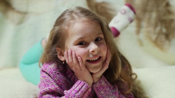 Beautiful little girl smiling at camera. Portrait of cheerful kid lying on couch - Video