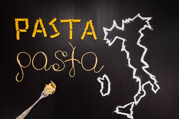 Words pasta made of cooked spaghetti and dry pasta on the black background with frame of country Italy written by chalk and fork - 写真・画像