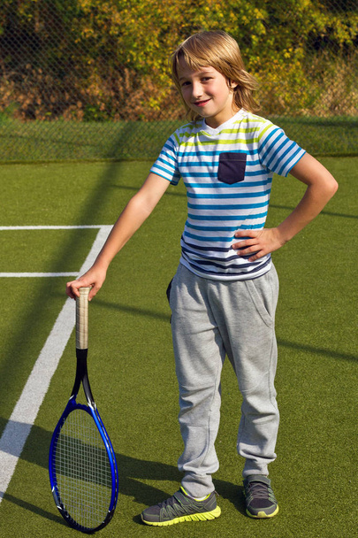 Хлопчик стоїть з тенісною ракеткою і м'ячем на подвір'ї
 - Фото, зображення