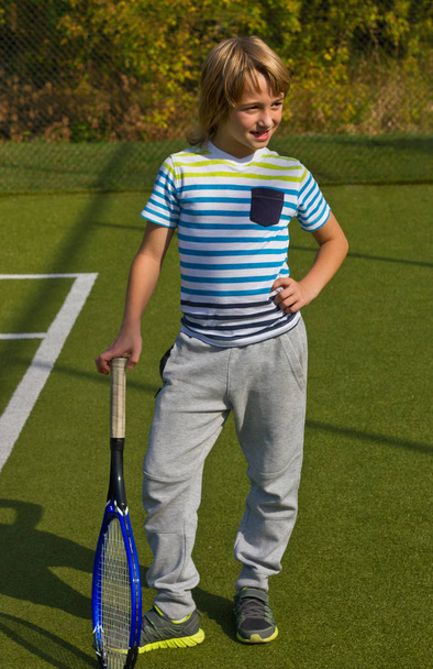 Αγόρι που στέκεται με ρακέτα του τένις και μπάλα στο γήπεδο - Φωτογραφία, εικόνα