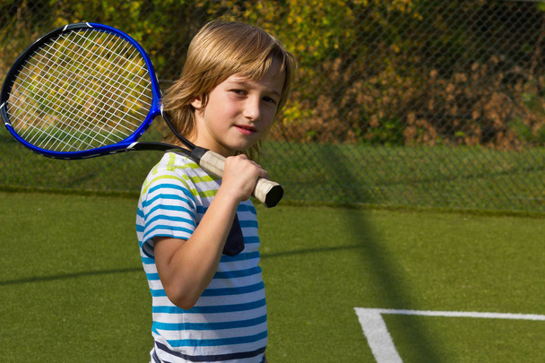 Niño de pie con raqueta de tenis y pelota en la cancha
 - Foto, Imagen