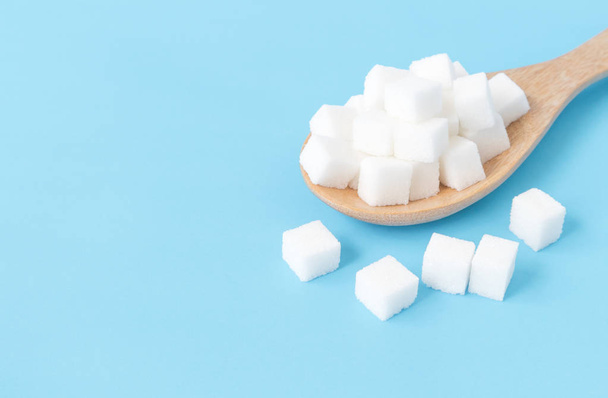 Closeup sugar cubes on wooden spoon white blue background - Photo, Image