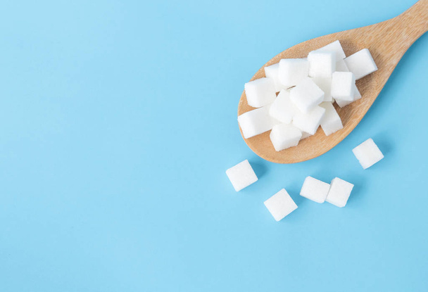Closeup cubos de açúcar vista superior na colher de madeira fundo azul branco
 - Foto, Imagem