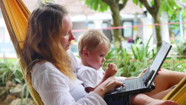 niña y niño trabajando en el ordenador portátil y el teléfono inteligente acostado en una hamaca
 - Metraje, vídeo