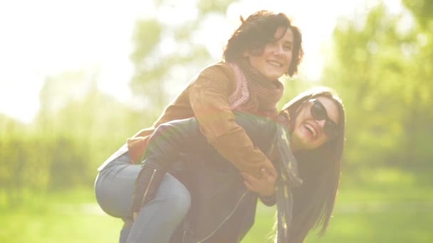 Šťastné ženy přátelé je má zábava venku těší slunečního záření v parku. Mladá žena s dlouhými vlasy a sluneční brýle je nést další jeden na její ramena na zelené trávě pozadí. - Záběry, video