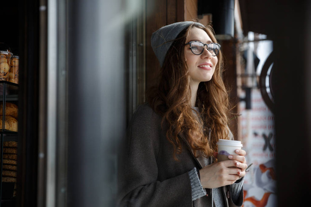 Happy attractive young woman thinking and drinking coffee outdoors - Foto, afbeelding