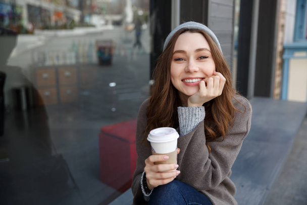 Ευτυχισμένη γυναίκα χαμογελαστή και πίνοντας τον καφέ στην πόλη - Φωτογραφία, εικόνα