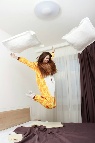 Funny girl in kigurumi pajamas jumping on the bed - 写真・画像