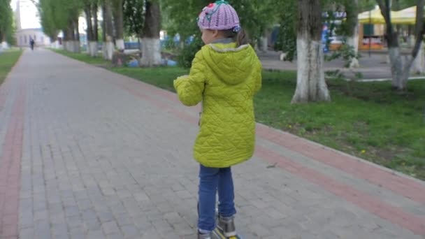 Little girl in green jacket riding a scooter. Shooting Steadicam. Slow motion - Felvétel, videó