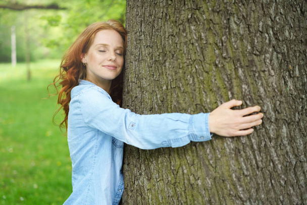 Ευχαριστημένος νεαρή γυναίκα αγκαλιάζει ένα μεγάλο δέντρο - Φωτογραφία, εικόνα