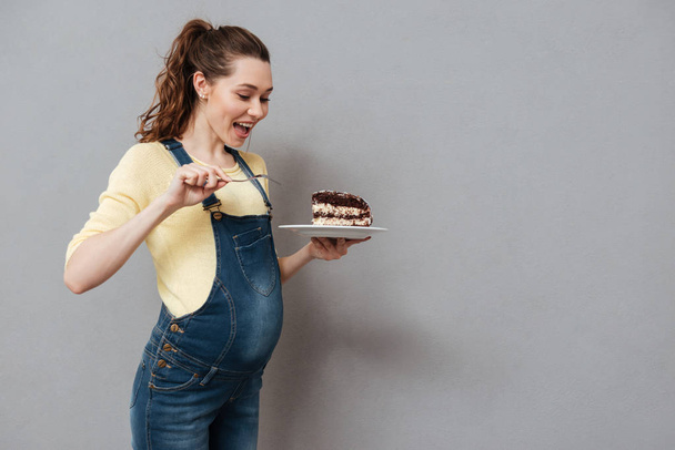 Portrait of an excited young pregnant woman eating chocolate cake - Foto, afbeelding
