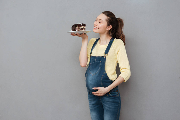 Happy pregnant lady holding sweet cake. Looking aside. - Foto, Imagem