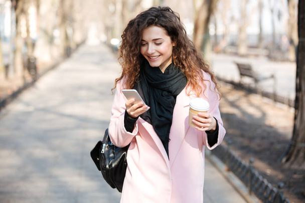 Cheerful woman using her phone in the sunny city street . - Foto, Imagen