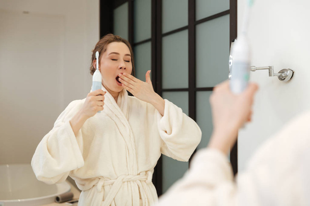 Сонная расслабленная женщина зевает и чистит зубы в ванной
 - Фото, изображение