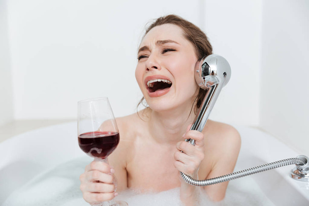 Sad woman with glass of wine crying in bathtub - Photo, image