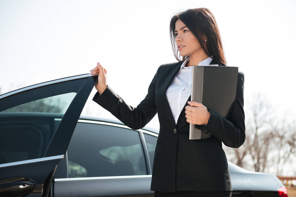 Businesswoman holding folder standing near the car - Fotó, kép