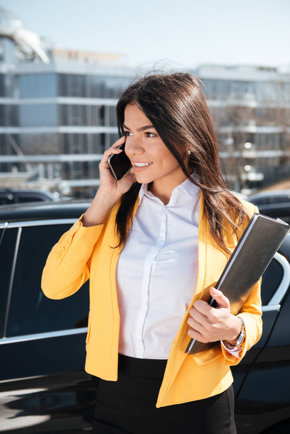 Happy businesswoman holding folder and talking on mobile phone outdoors - Foto, Imagen