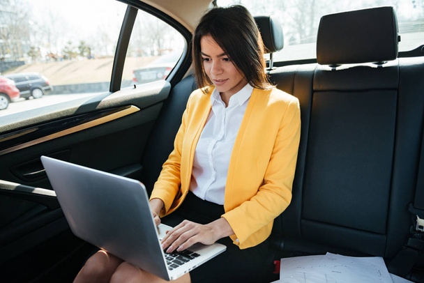 Businesswoman sitting on back seat of car and working - Фото, зображення