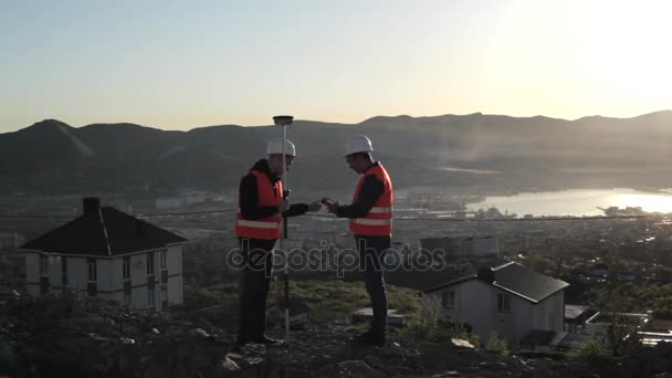 Dos topógrafos en cascos que realizan mediciones geodésicas en la cima de la montaña
 - Metraje, vídeo