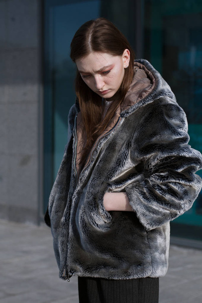 A beautiful and fashionable girl in a fur coat walks in the city on a sunny day - Foto, afbeelding