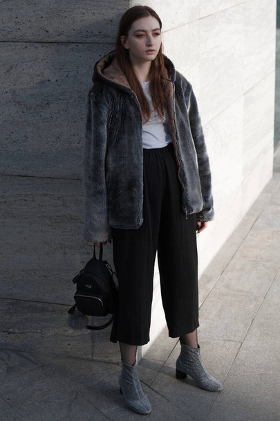 A beautiful and fashionable girl in a fur coat walks in the city on a sunny day - Foto, afbeelding
