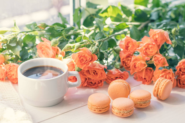 Macarrones de naranja, taza de café y rosas frescas
 - Foto, imagen